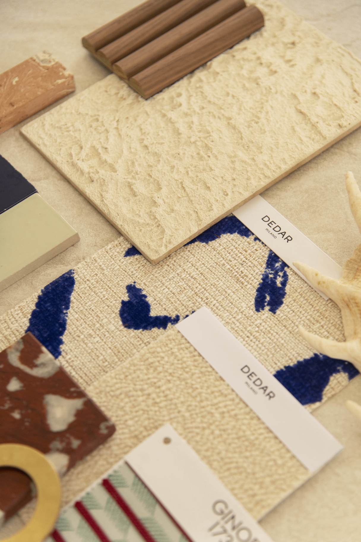 Close-up of curated materials — travertine, walnut, marble and printed fabric